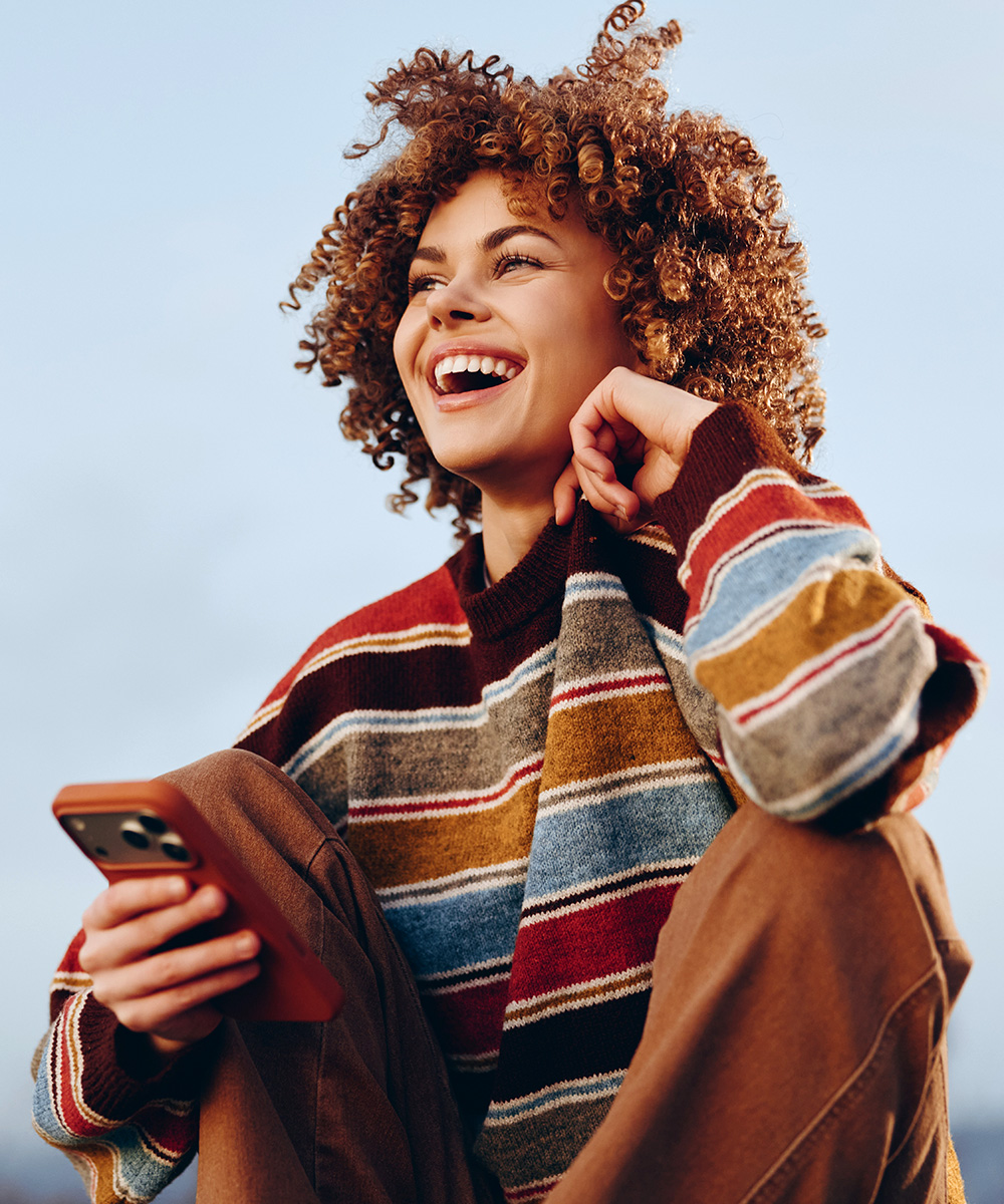 Profissional jovem em recolocação, sorrindo com o celular na mão